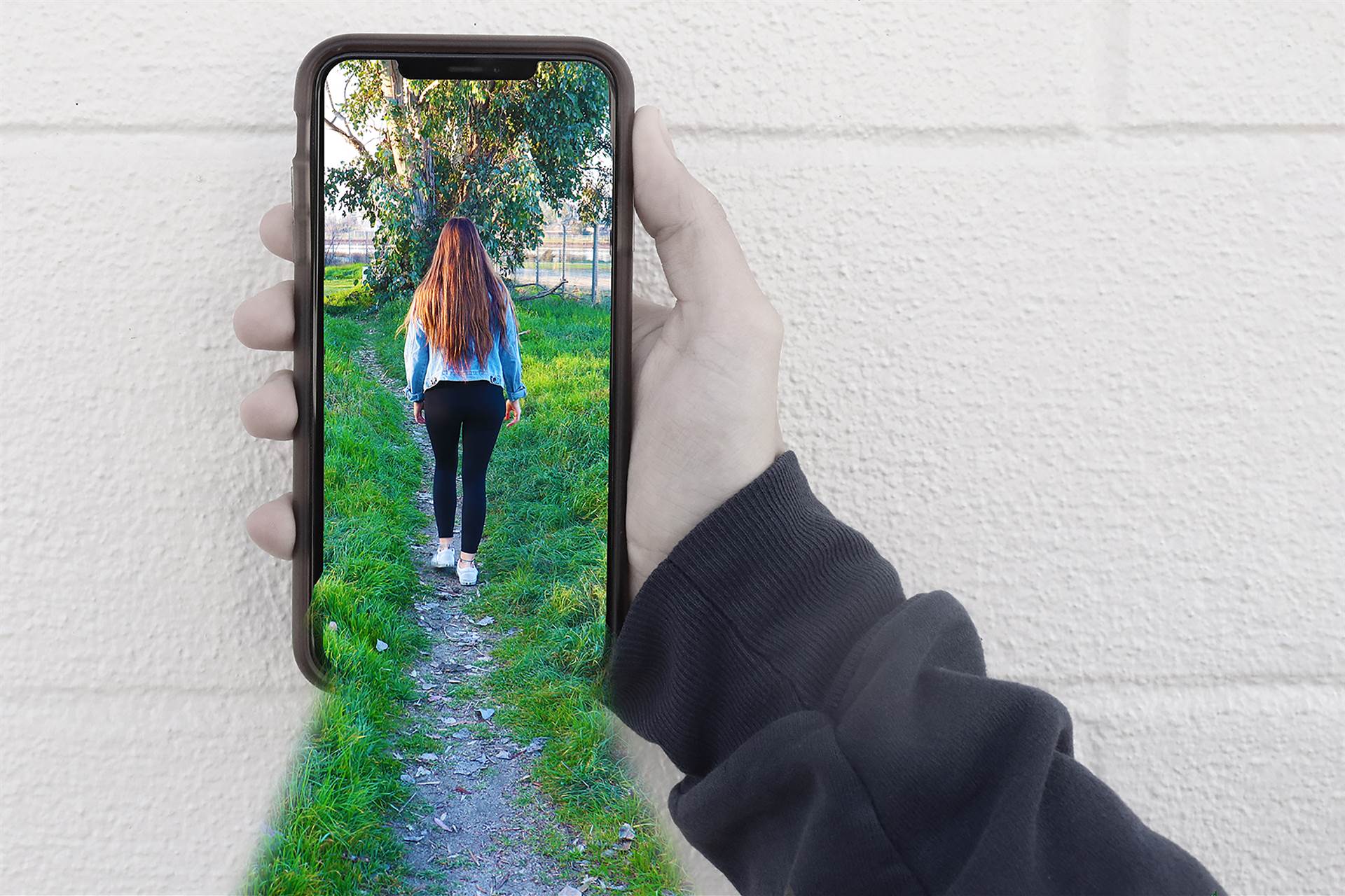 Photo of a boy holding phone with girl walking down a path through phone