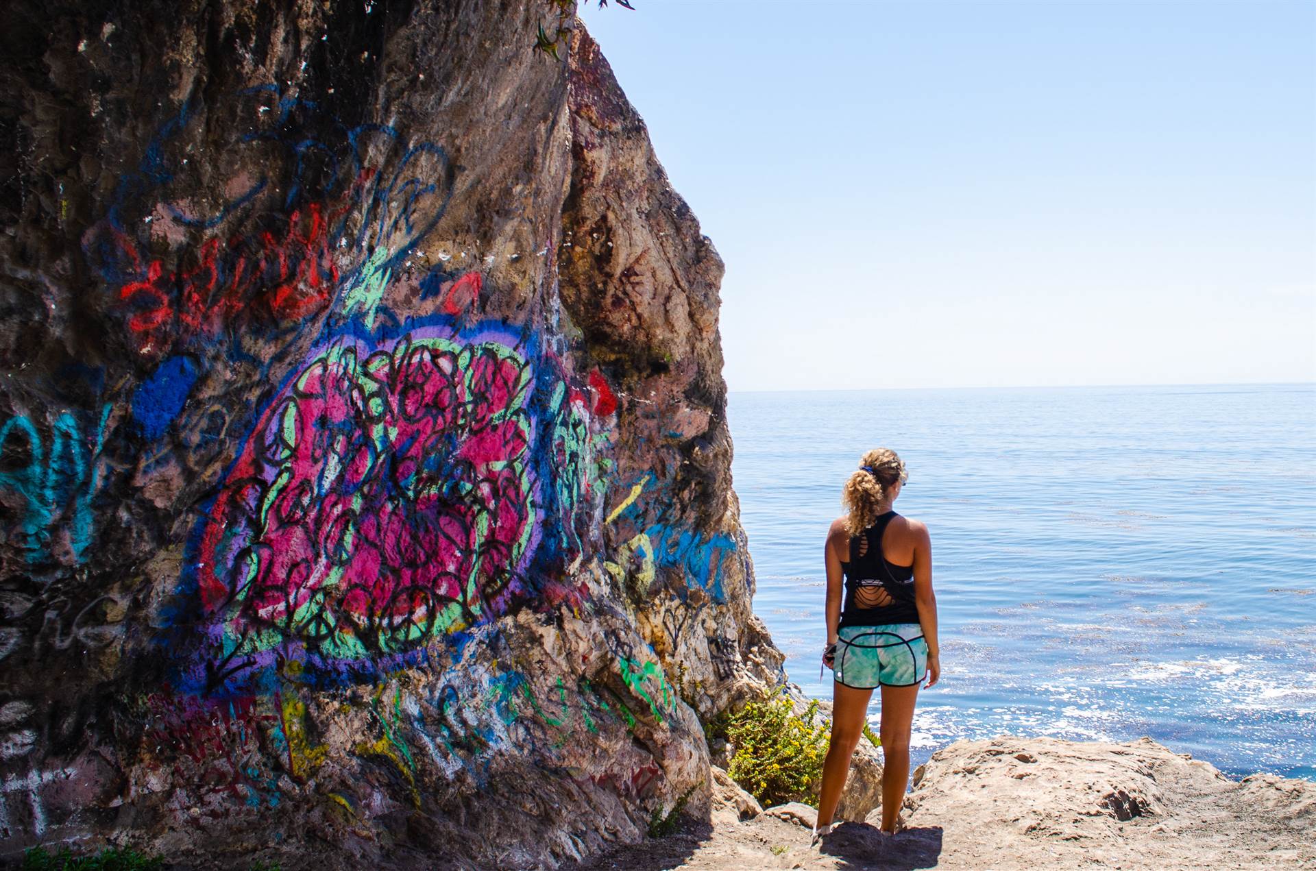 Girl looking at ocean with graffiti rock next to her