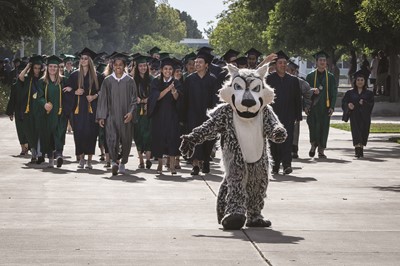 Students in caps and gowns walking behind Clovis East T-Wolf